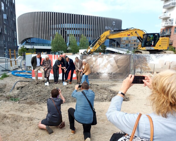 Syv mennesker står med spader i byggegrunden foran Royal Arena på Amager