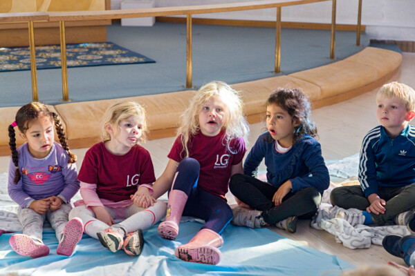 Fem børn på ca. 5 år år sidder i en halvcirkel i en kirke og er en del af Børnetjenesten