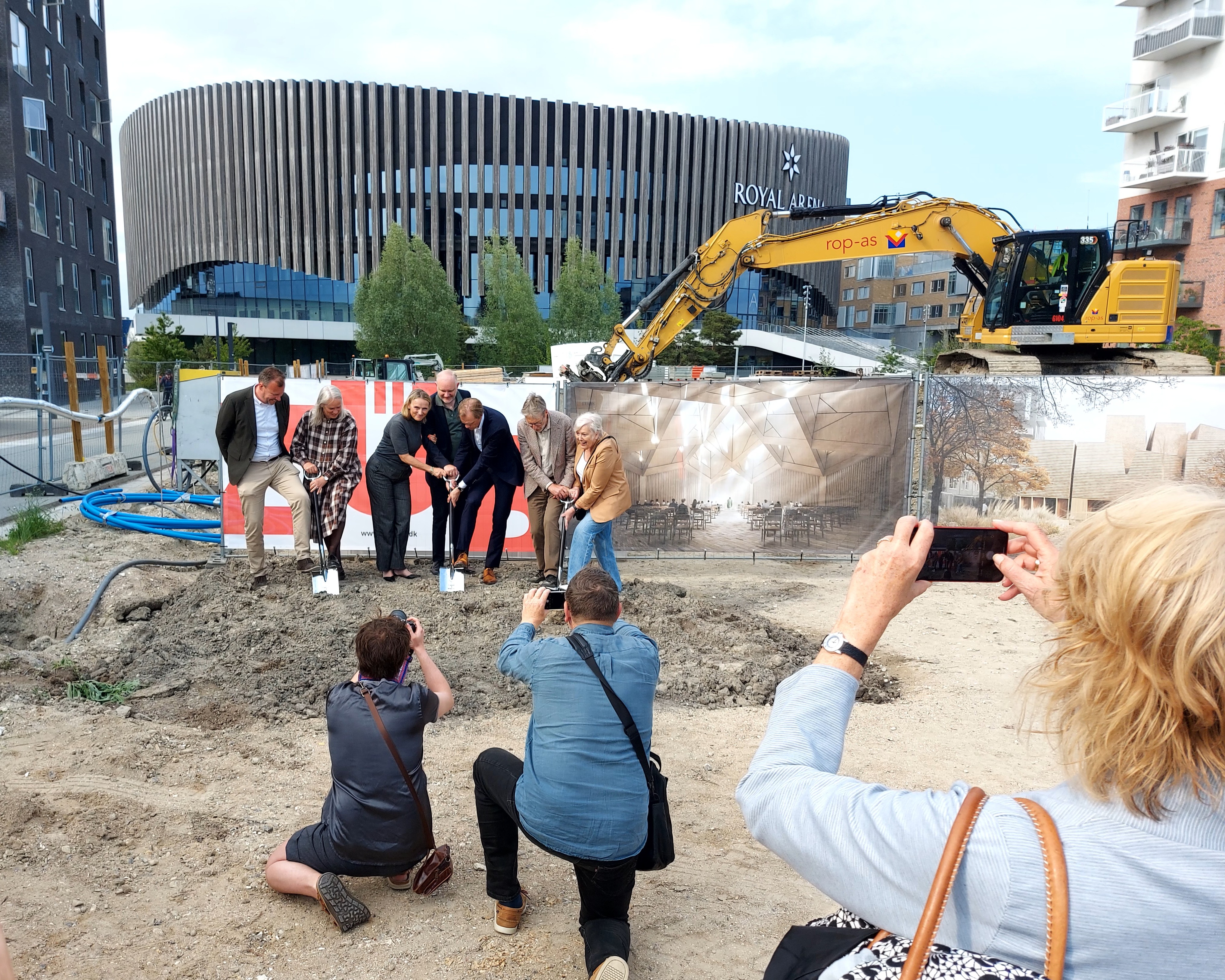 Syv mennesker står med spader i byggegrunden foran Royal Arena på Amager